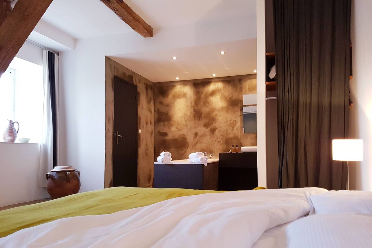 Habitación de hotel con cama, mesita de noche con lámpara, ventana con cortinas y pared con textura.