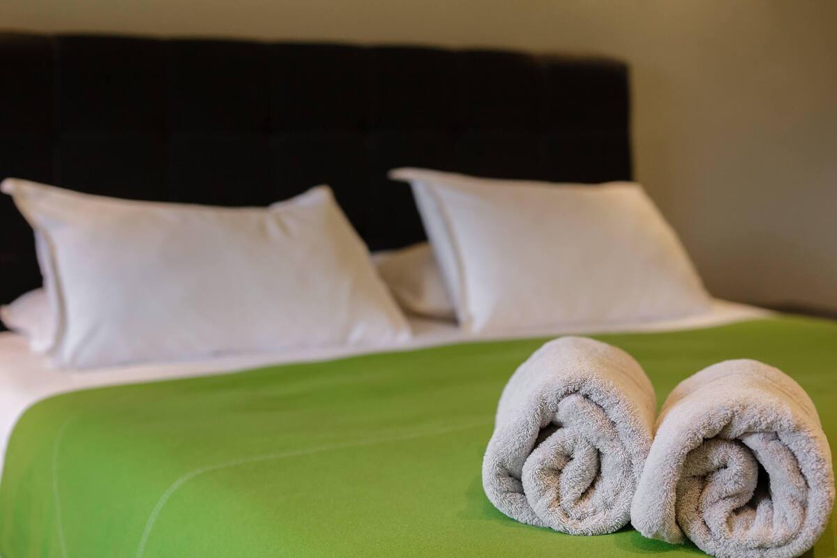 Una cama bien hecha con almohadas blancas y colcha verde.