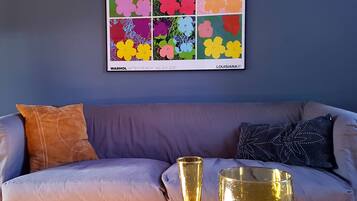 A living room with a sofa, two cushions, a framed artwork, and two glasses on a table.