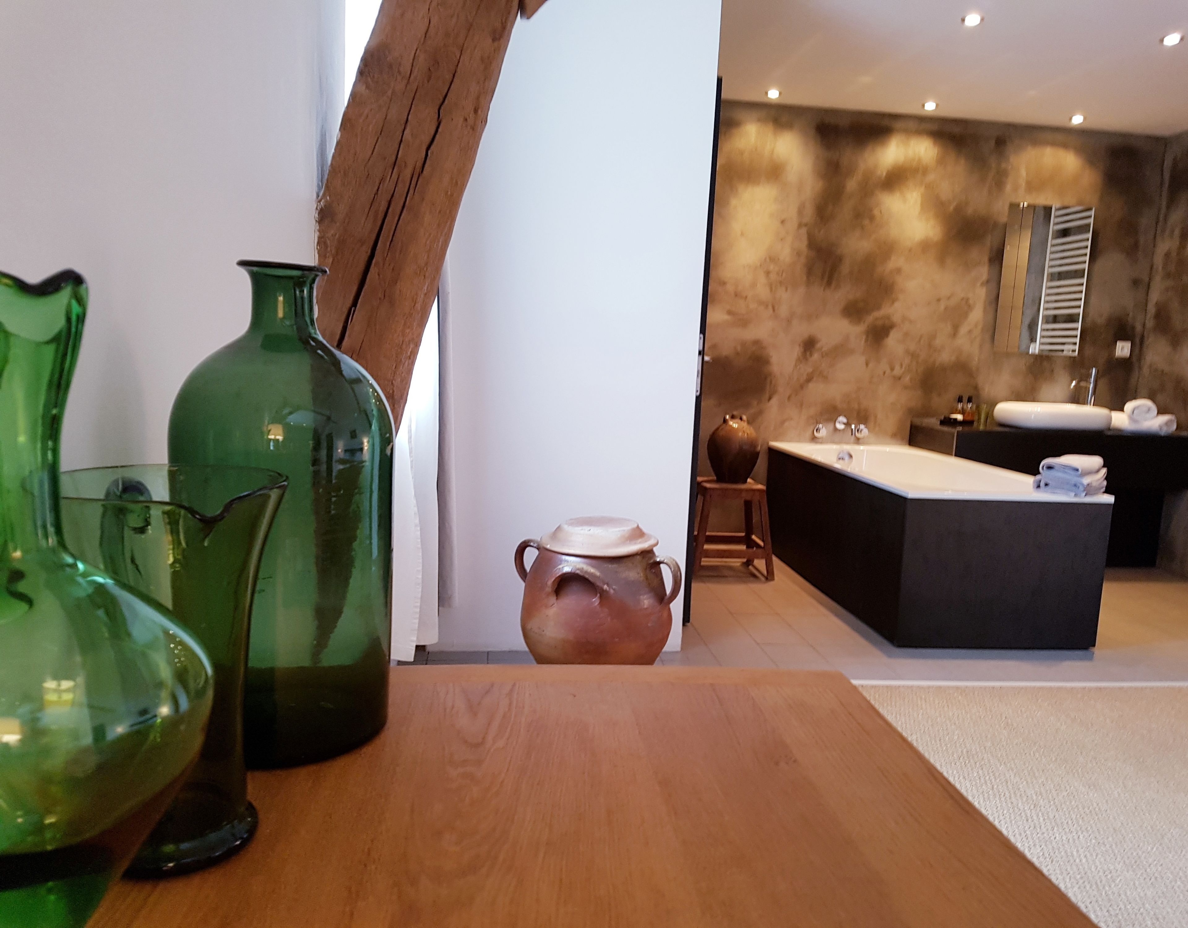 A modern bathroom with a large bathtub, a sink, and a vanity. There are two green glass vases on a wooden table in the foreground.