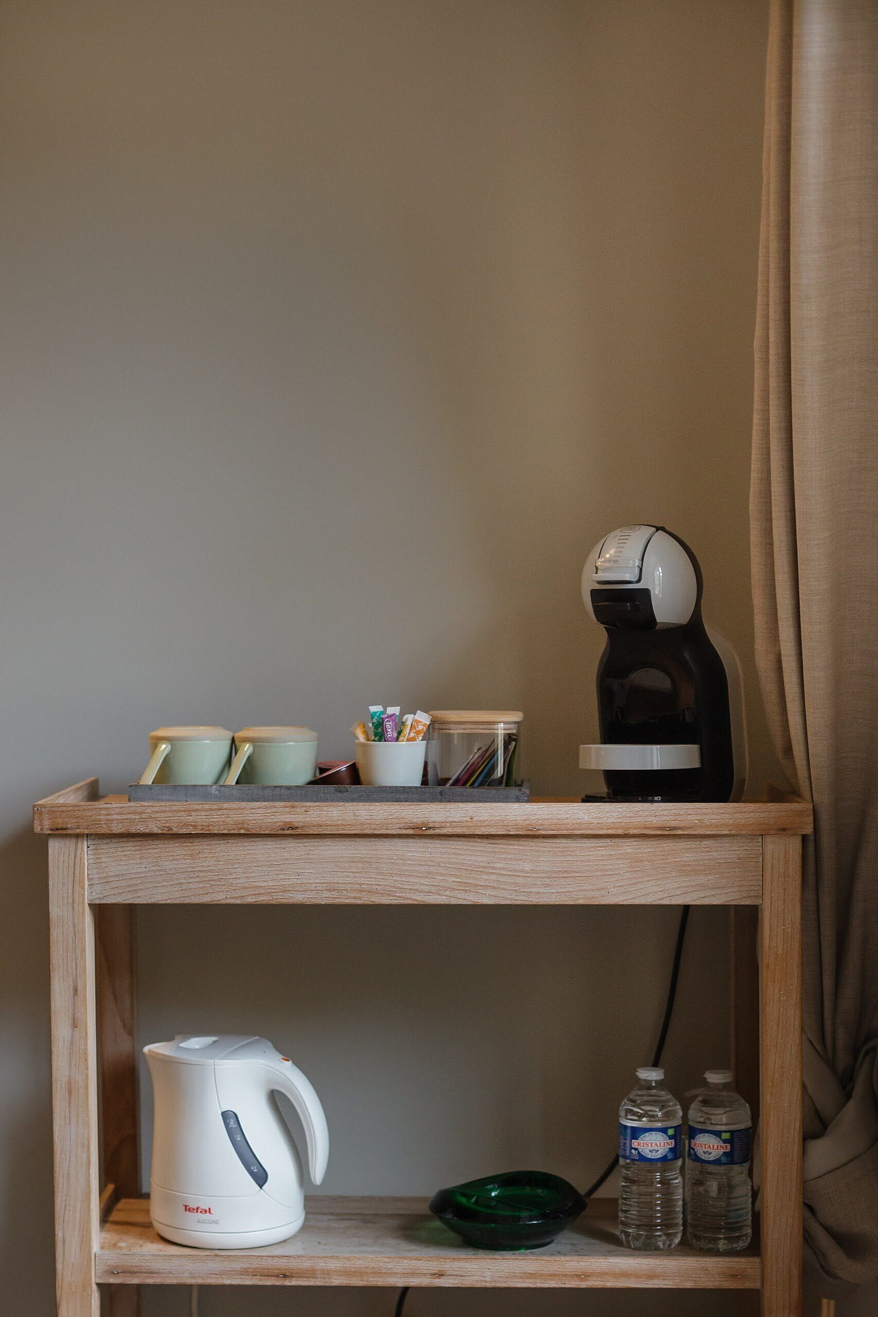 Ein Holzregal mit einem weißen Wasserkocher, zwei Wasserflaschen, einer grünen Schüssel und einer Kaffeemaschine.