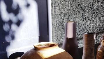 Um vaso grande e texturizado sobre uma mesa, com outros vasos e uma parede texturizada ao fundo.