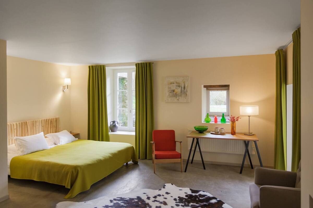 Una habitación de hotel con una cama, un escritorio, una silla, un ventanal con cortinas, una lámpara y un tapiz de cuero de vaca.