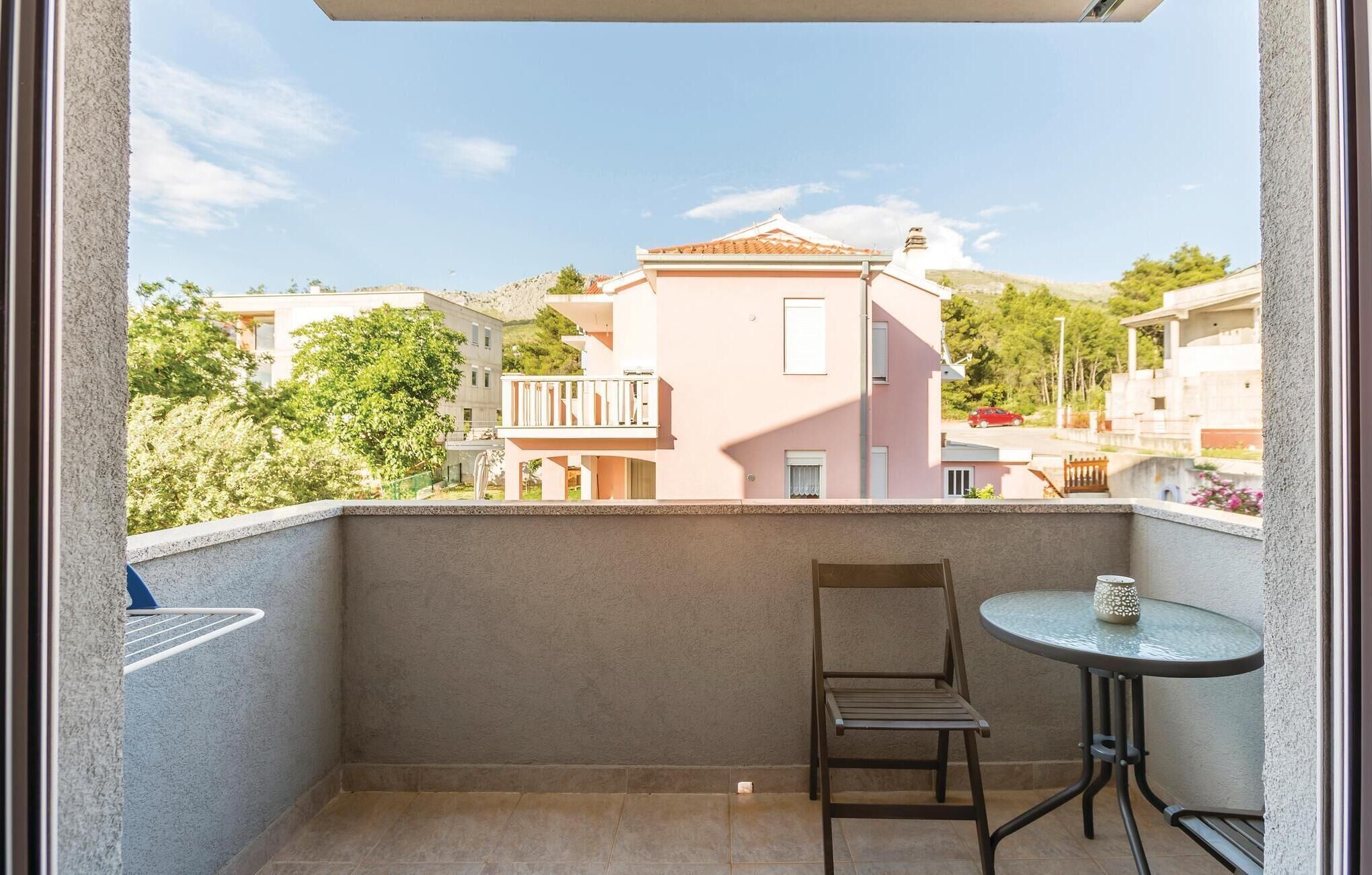 A balcony with a chair and a small table, overlooking a residential area with buildings and trees.