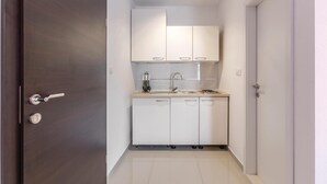 Une cuisine de taille réduite, avec des meubles blancs, un évier en acier inoxydable et une porte en bois foncé.