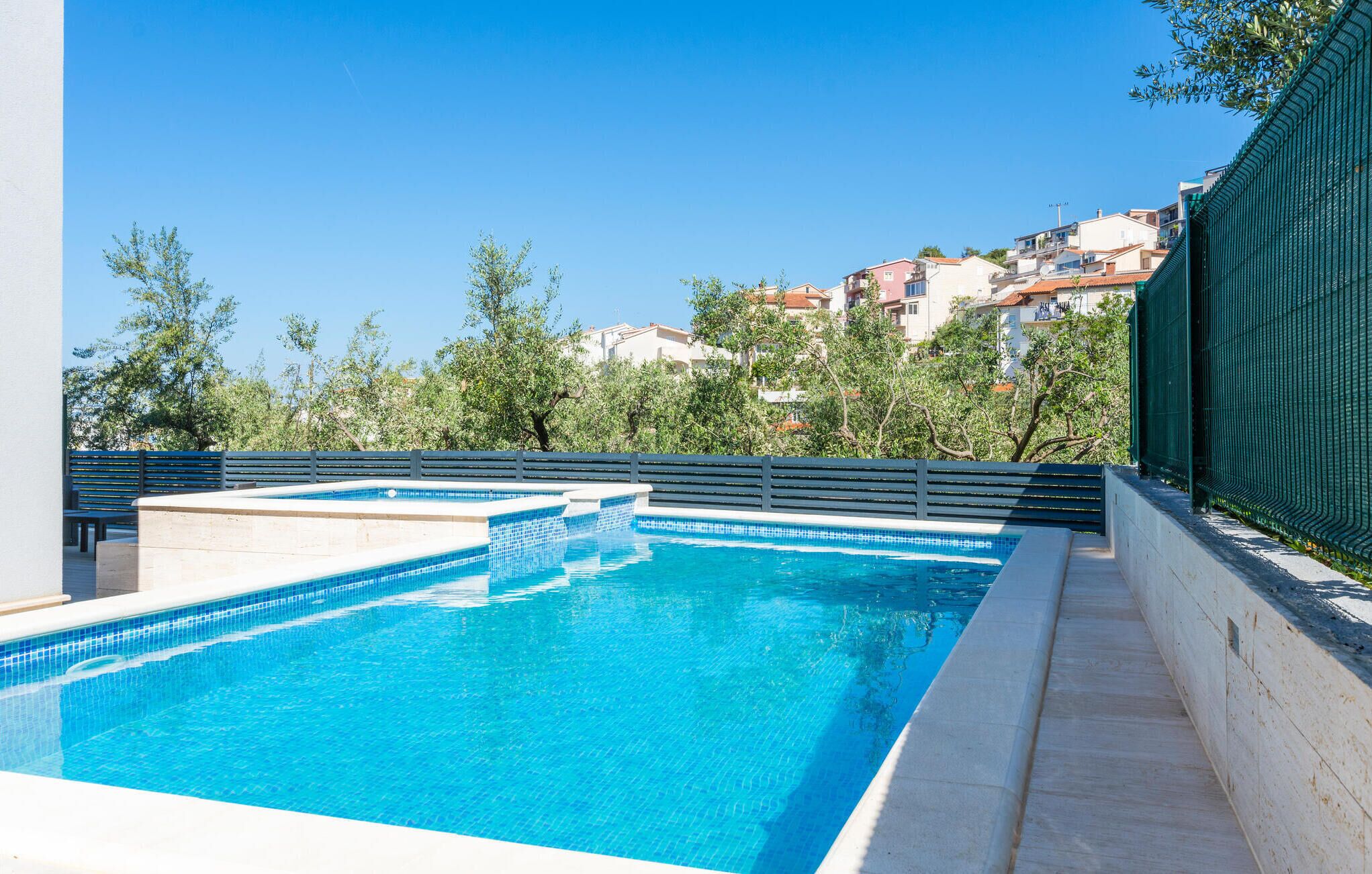 Une piscine à l’eau d’un bleu cristallin, entourée d’un petit muret en pierre et d’une clôture en métal.