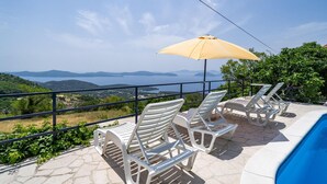 A terrace with white plastic lounge chairs and a yellow umbrella overlooking a body of water and distant mountains. - Gorgeous home in Slano (Slano)