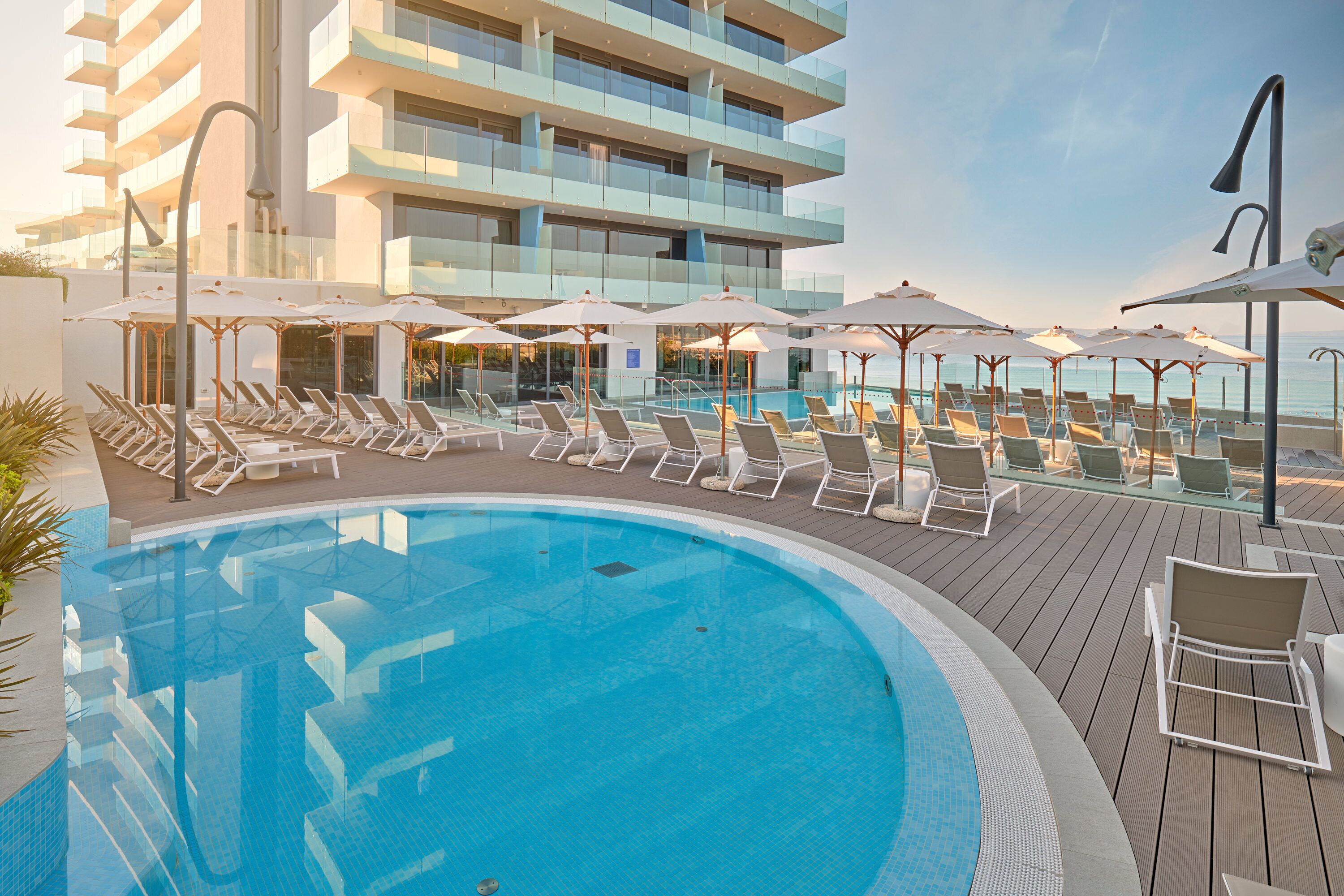 A poolside area with lounge chairs and umbrellas, a clear blue pool, and a modern building in the background.