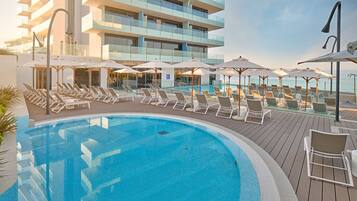 A poolside area with lounge chairs and umbrellas, a clear blue pool, and a modern building in the background.