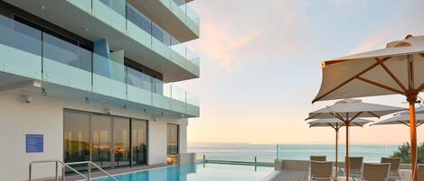 A modern hotel with a rooftop infinity pool, outdoor seating, and a view of the ocean.