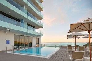 A modern hotel with a rooftop infinity pool, outdoor seating, and a view of the ocean.