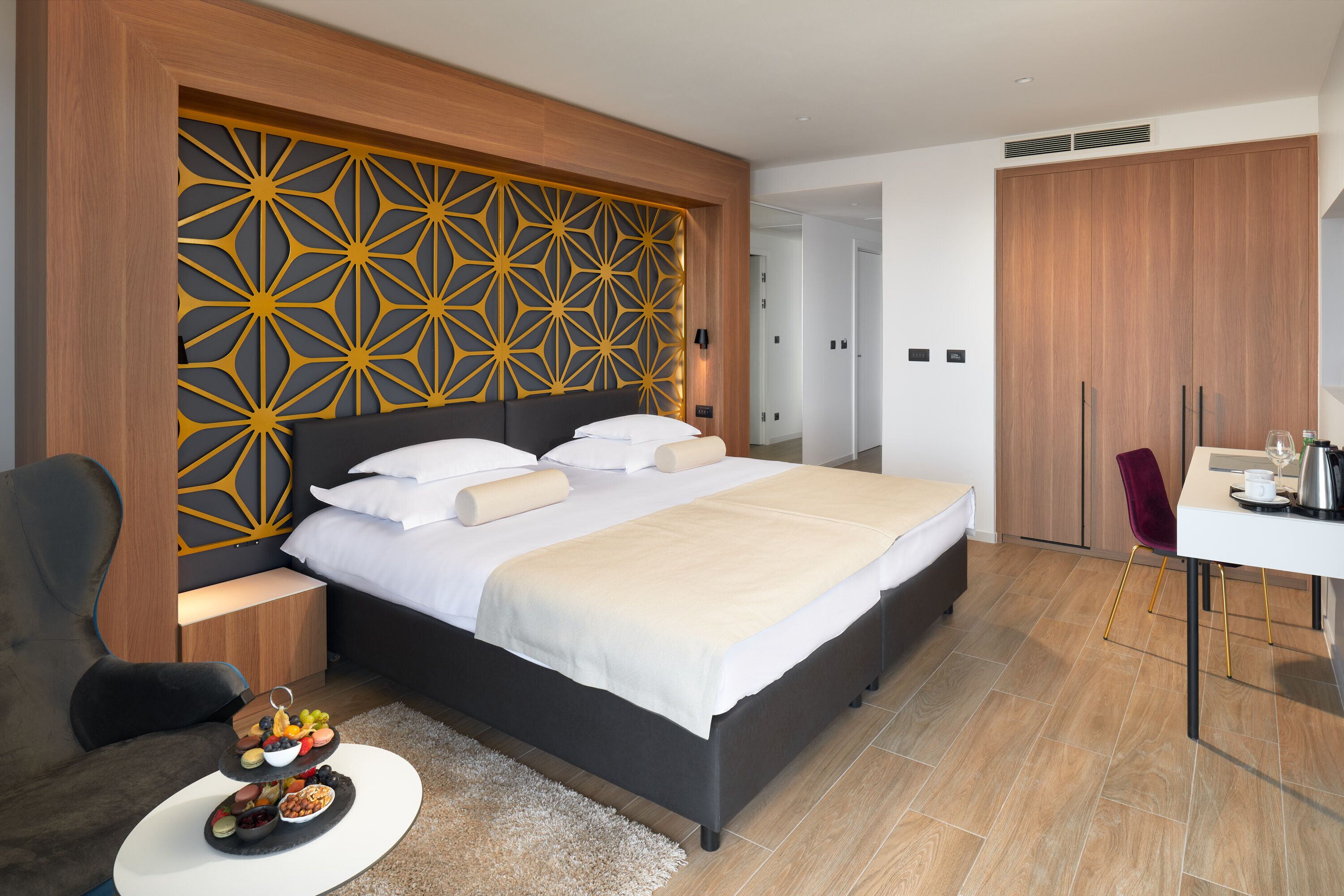 A modern hotel room with a large bed, a desk, and a wardrobe.