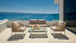 A balcony with two wicker chairs, a table with food and drinks, and a view of the sea.