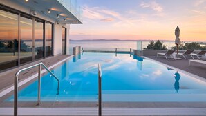 A modern infinity pool with clear blue water, surrounded by lounge chairs and a glass railing.