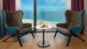 A room with two chairs facing a balcony with a view of the sea.