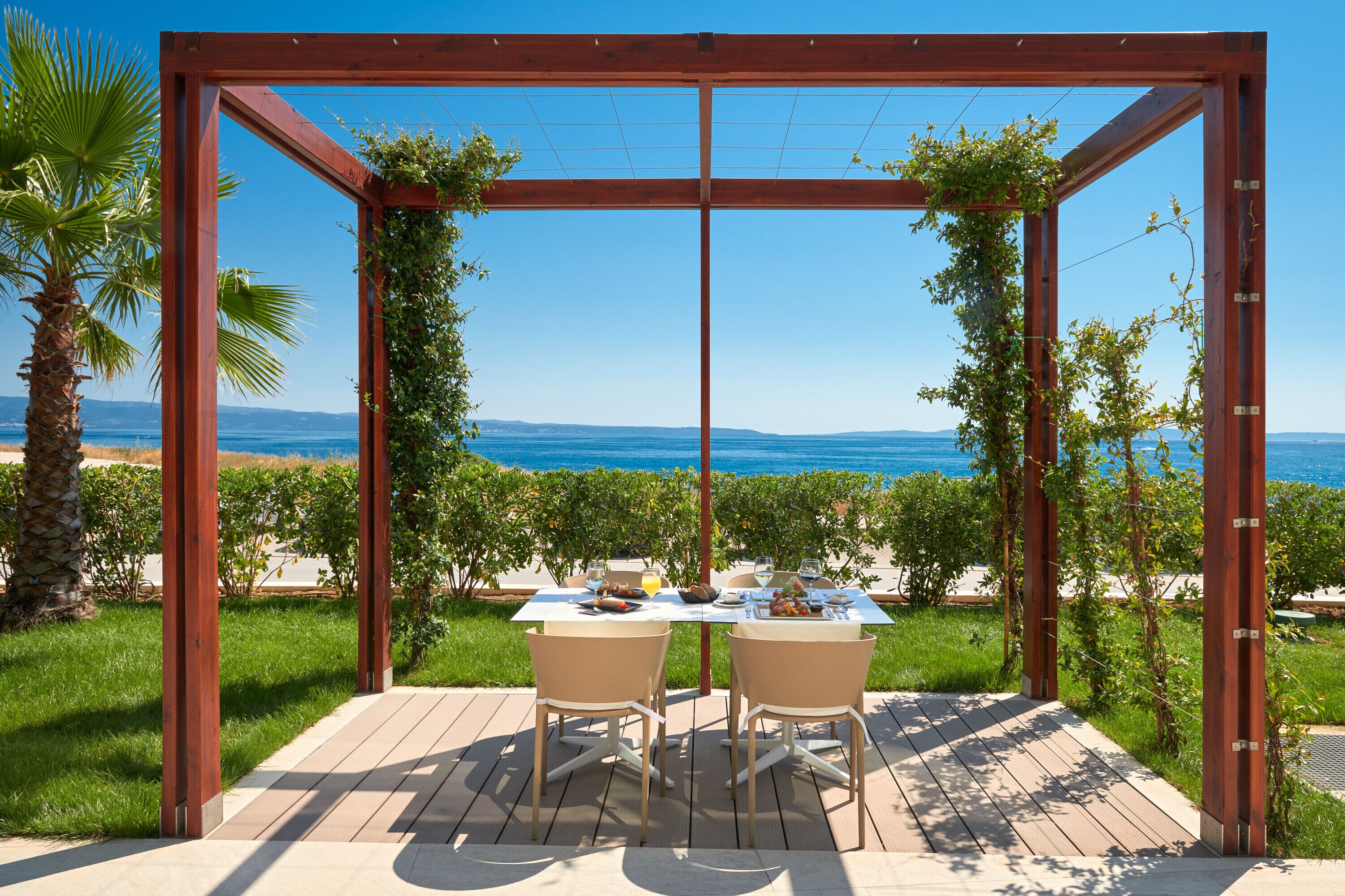 A wooden pergola with a table set for two, overlooking a beach and ocean.