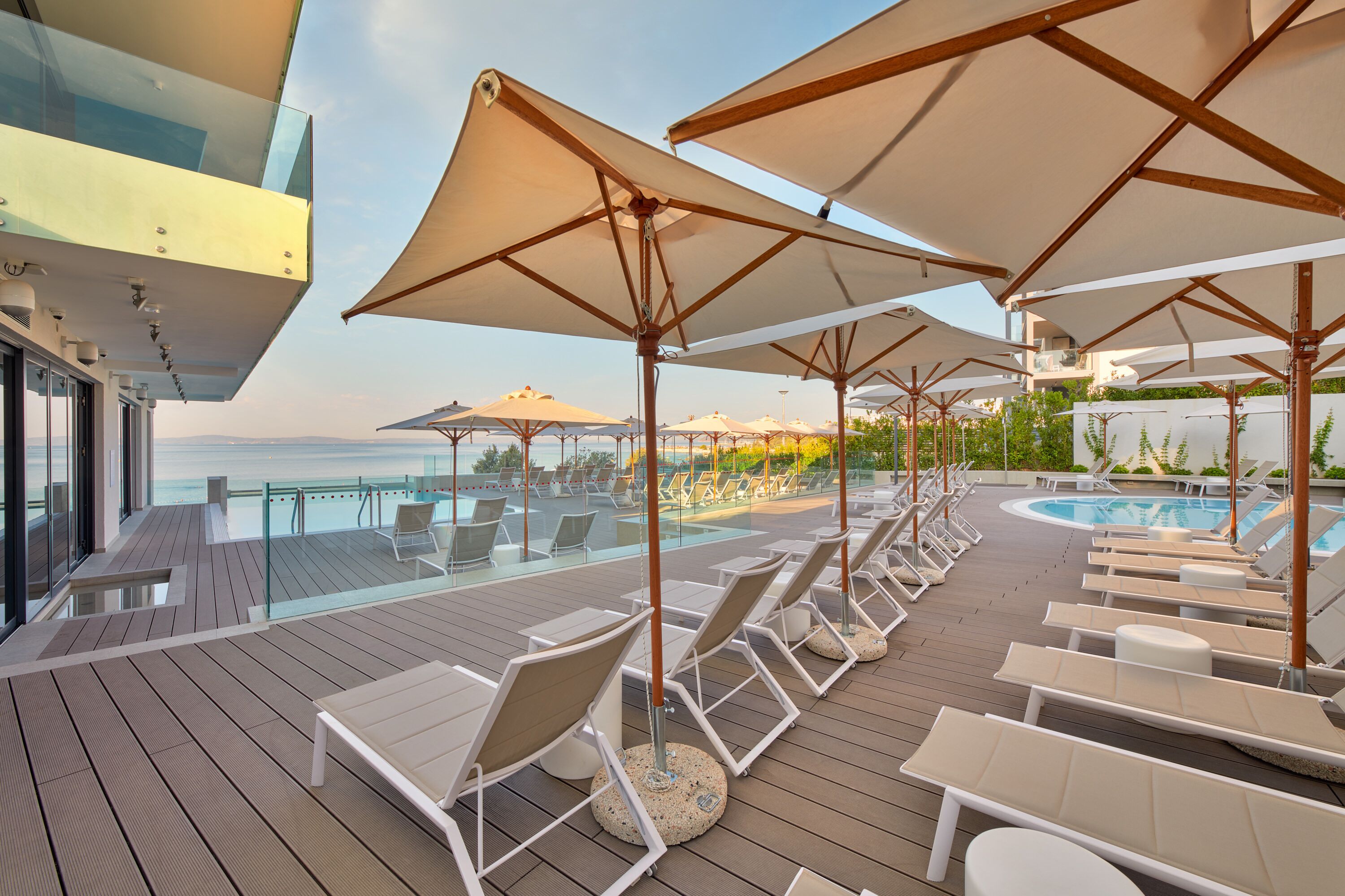 A deck with sun loungers and umbrellas overlooking a pool.