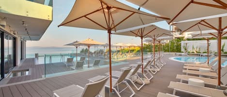 A deck with sun loungers and umbrellas overlooking a pool.