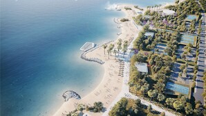 An aerial view of a coastal area with a beach, a swimming pool, and a park area.