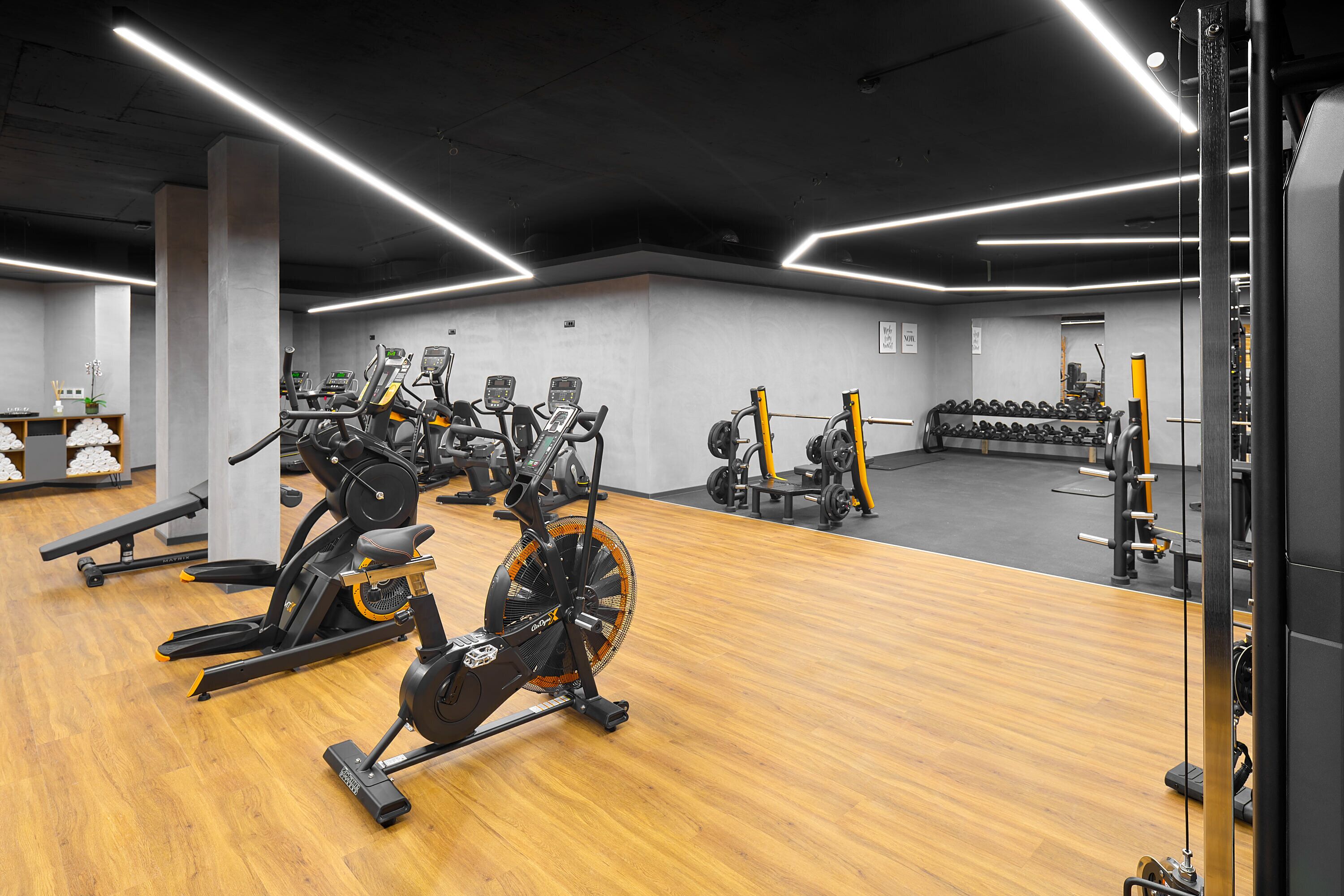 Uma academia com equipamentos de ginástica, piso de madeira e iluminação brilhante.