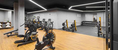 A gym with exercise equipment, wooden flooring, and bright overhead lighting.
