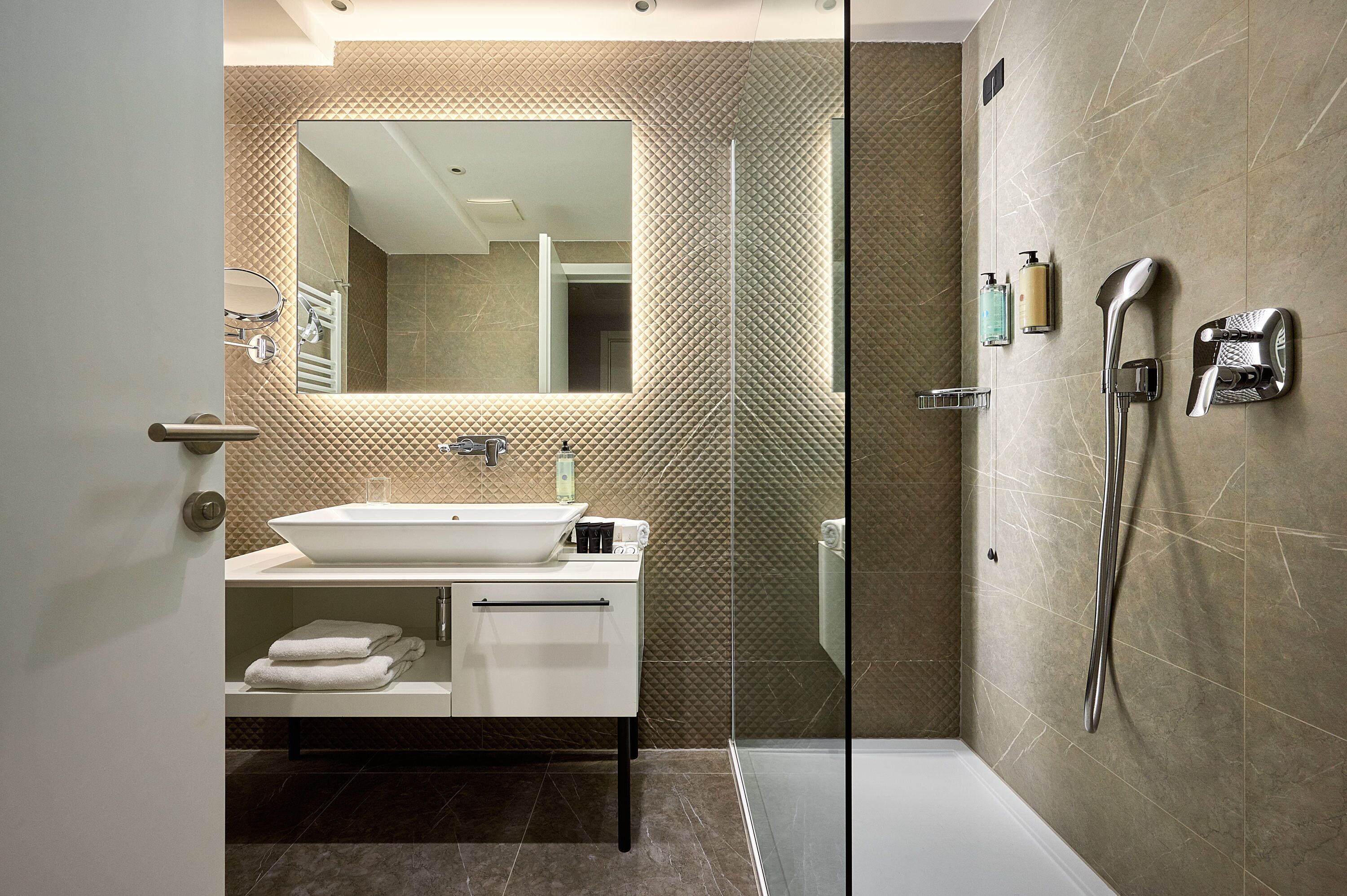Une salle de bain moderne avec un grand miroir, un lavabo blanc et un espace douche.