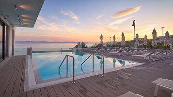Relax by the rooftop pool overlooking the sea and distant mountains, surrounded by lounge chairs and umbrellas.