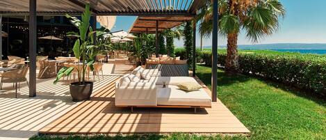 A covered outdoor seating area with a wooden deck, a sofa, and potted plants.
