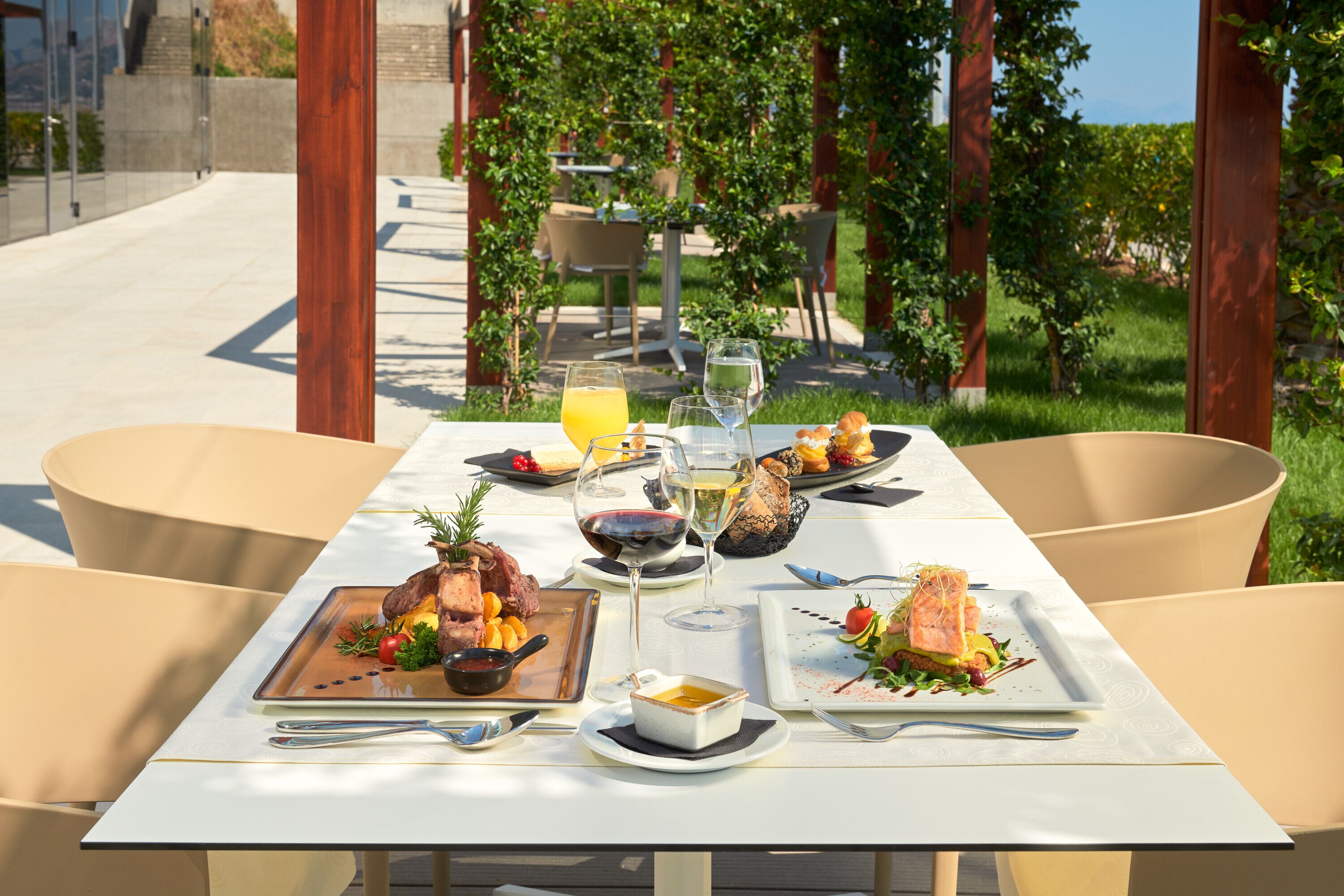 Une table à manger installée à l’extérieur, où sont servis divers plats, notamment des fruits de mer et des légumes, dans un jardin agrémenté de chaises et offrant une vue sur le paysage.