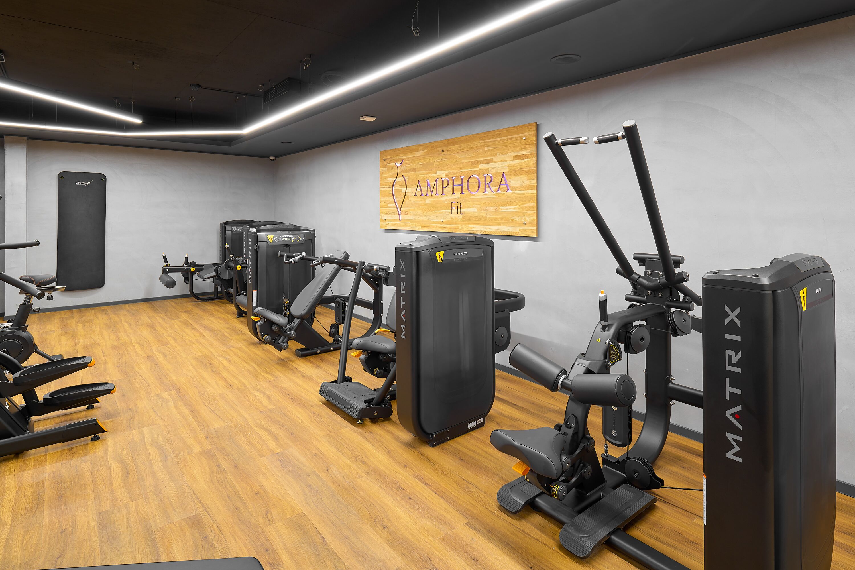 Un gimnasio con diversas máquinas de ejercicio, un letrero de madera en la pared y un saco de boxeo negro colgado.