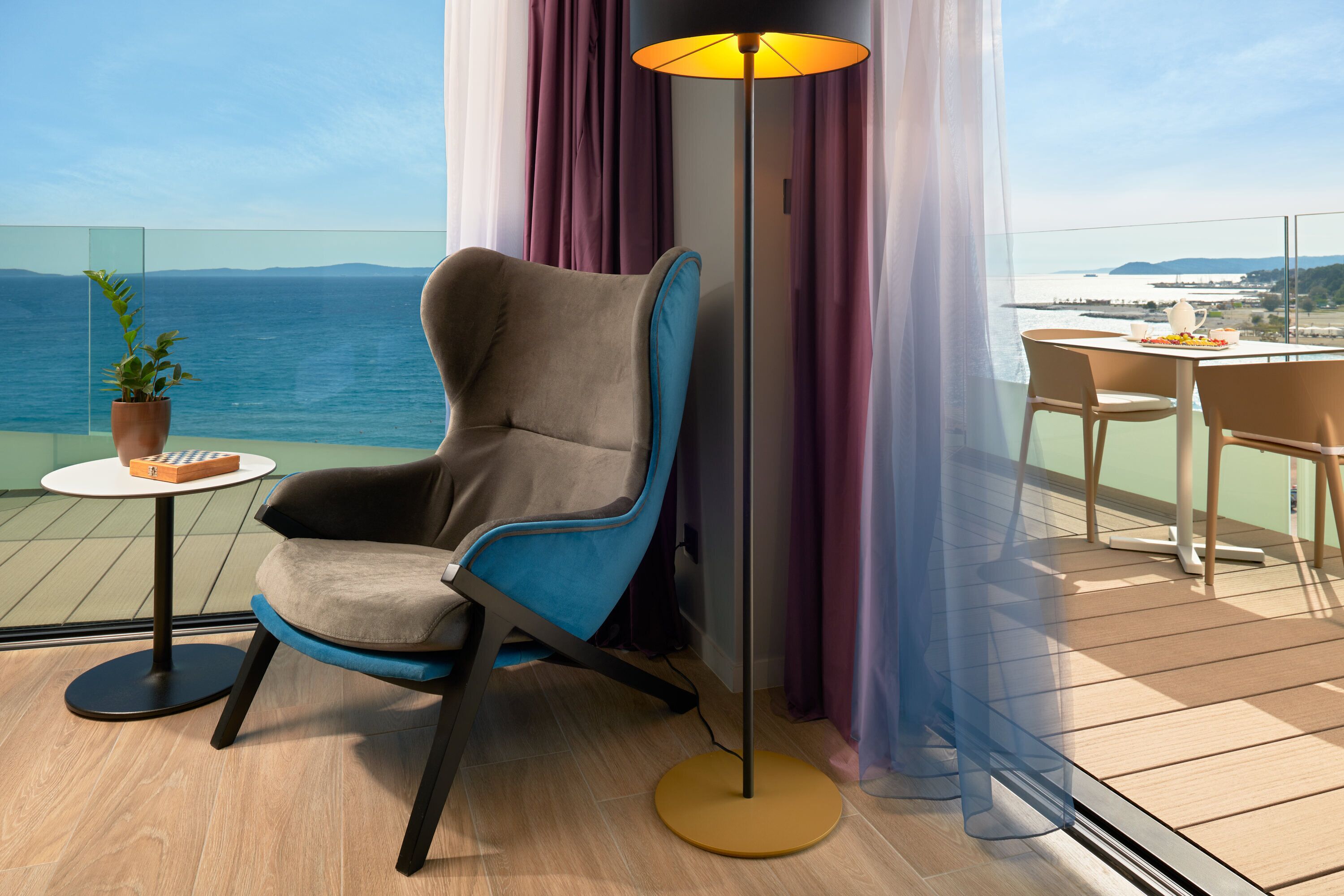 A modern chair with a side table, a floor lamp, and a view of the sea.