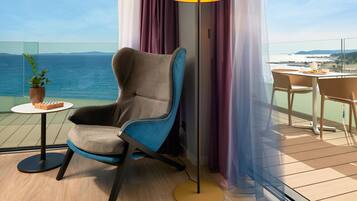 A modern chair with a side table, a floor lamp, and a view of the sea.
