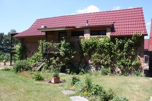 A brick house with a red-tiled roof, a front porch, and a garden with various plants and flowers. - Apartment with winter garden and lake view - Ferienhof Löschebrand (Bad Saarow)
