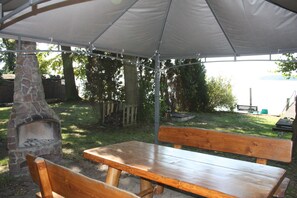 An outdoor patio area with a stone fireplace, wooden benches, and a canopy. - Apartment with winter garden and lake view - Ferienhof Löschebrand (Bad Saarow)