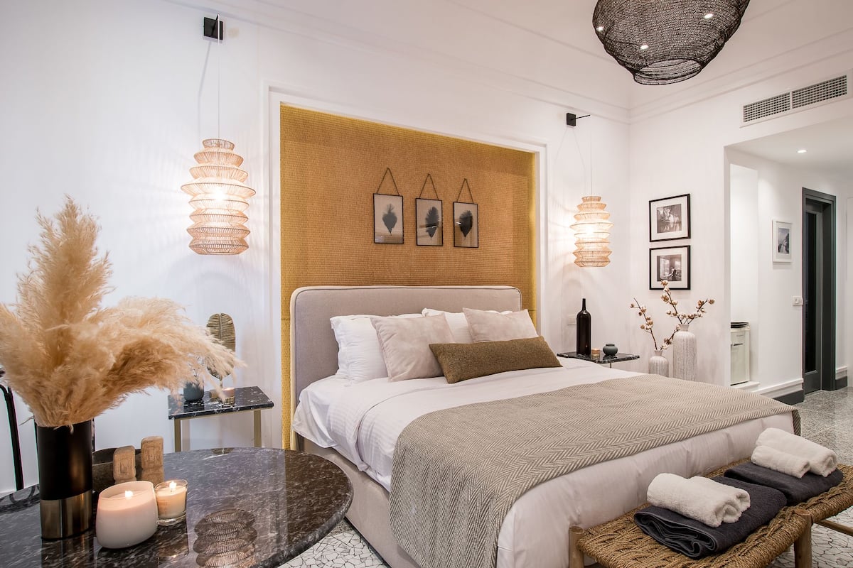 Un dormitorio moderno con una cama grande, mesitas de noche, un espejo redondo y un panel decorativo en la pared.