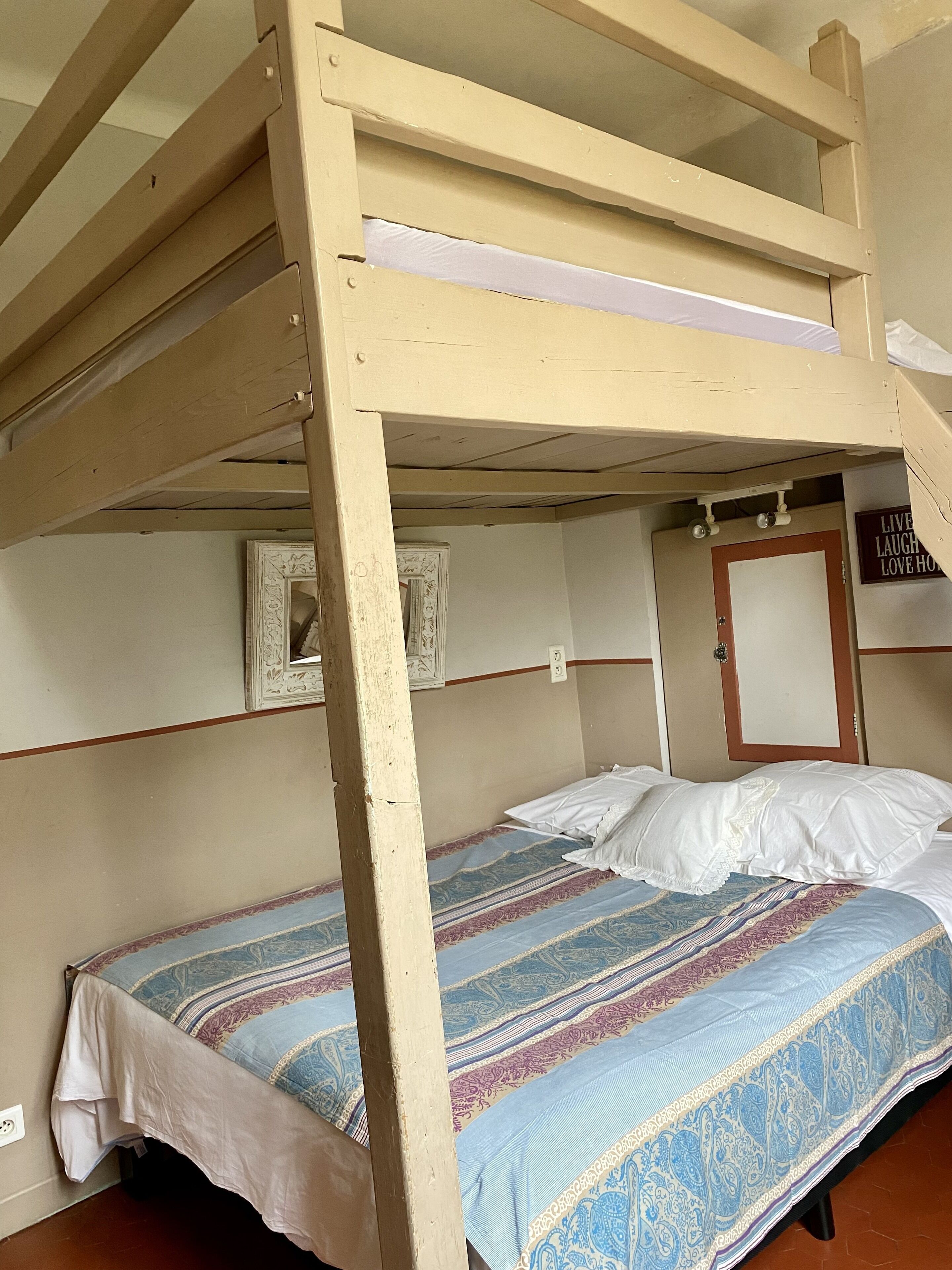 Un lit superposé avec une couvre-lit à motifs, un miroir et un mur orné d’une enseigne.