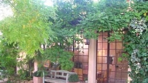 A garden area with a bench, a potted plant, and a building with a glass door. - Authentic farmhouse with large swimming pool, near Aix en Provence (Pourcieux)