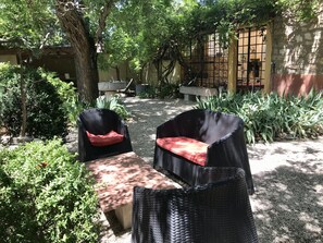 An outdoor seating area with wicker chairs and a table, surrounded by greenery and a stone wall.