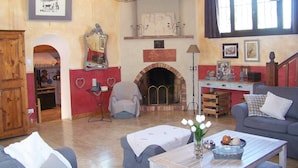 A cozy living room with a fireplace, a dining area, and a kitchen visible through an archway. - Authentic farmhouse with large swimming pool, near Aix en Provence (Pourcieux)