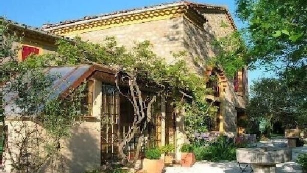 A rustic stone building with a tiled roof, a wooden door, and a small garden area with potted plants and a stone bench. - Authentic farmhouse with large swimming pool, near Aix en Provence (Pourcieux)