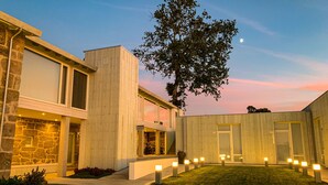 A modern building with a stone facade, a large tree, and a well-lit courtyard. - Hotel Nande (As Neves)