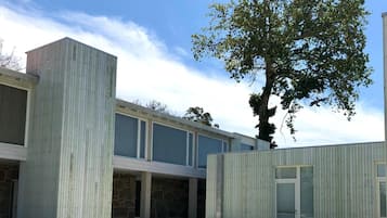 Un edificio moderno con techo plano, ventanas amplias y un patio ajardinado con escalones que conducen a la entrada.