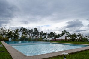 A rectangular swimming pool with a concrete edge, surrounded by grass and trees. - Hotel Nande (As Neves)
