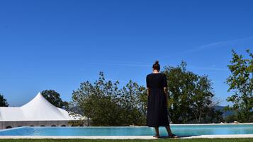 Una persona de pie junto a una piscina, con una carpa blanca y árboles al fondo.