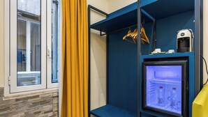A compact hotel room with a built-in mini-fridge, a coffee maker, and a window with curtains. - Seven (Rome)