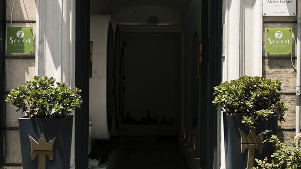 A building entrance with a dark interior, two potted plants with crown-shaped decorations, and a sign for Atelier Ferrari Bridal. - Seven (Rome)