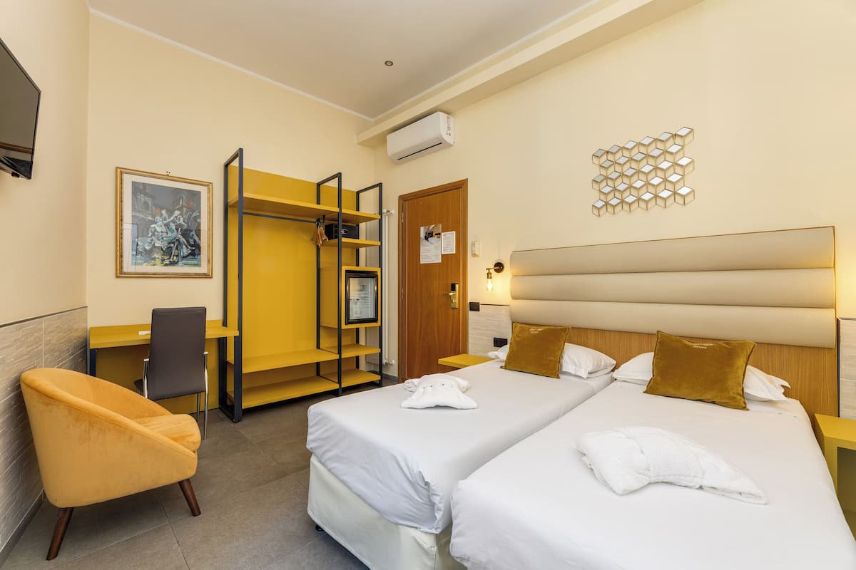 A hotel room with two beds, a desk, a chair, and a wardrobe.