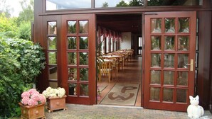 A building with large glass doors leading to an indoor dining area with wooden tables and chairs. - Willischza (Burg (Spreewald))