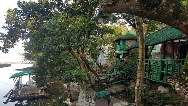 A riverside walkway with a wooden dock, stone walls, and a green-roofed structure. - Nature Green Forest Resort (Baler)