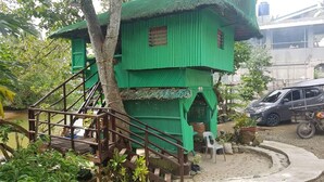A green treehouse with a wooden staircase leading up to it, surrounded by lush greenery. - Nature Green Forest Resort (Baler)